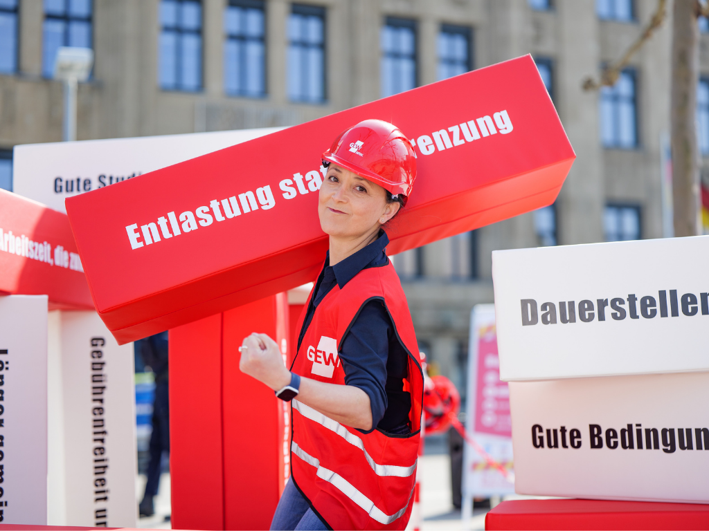 Ayla Çelik, Vorsitzende der GEW, trägt den Baustein "Entlastung statt Entgrenzung" und zeigt mit dem "starken Arm": Die GEW kämpft für die Beschäftigten. 